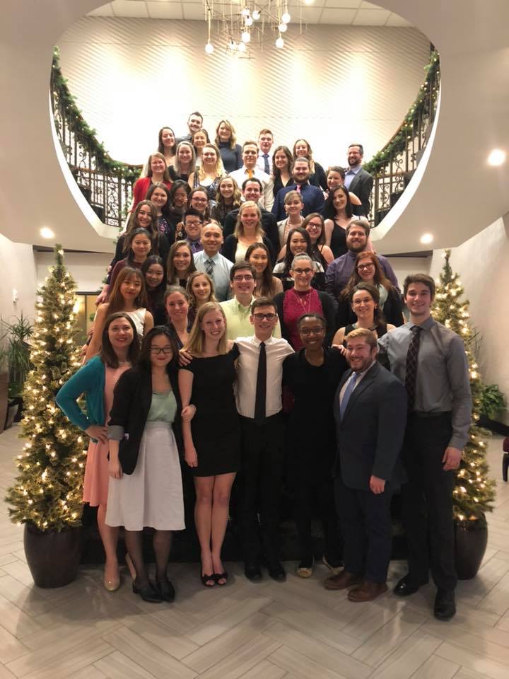 Kappa Psi members pose together amidst holiday lights on a staircase