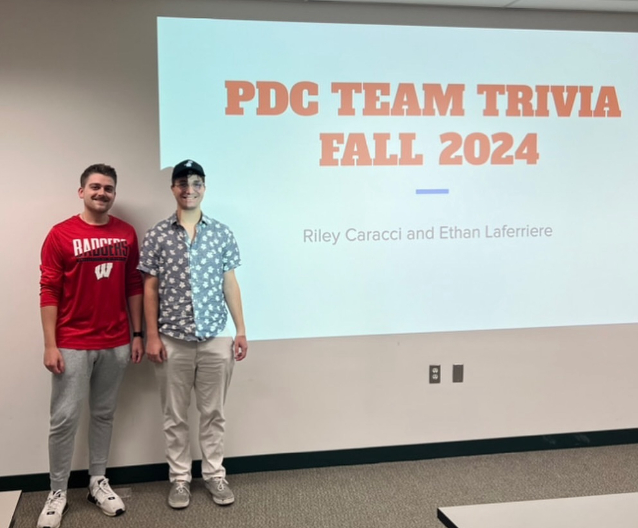 Two students standing in front of projector presentation for trivia