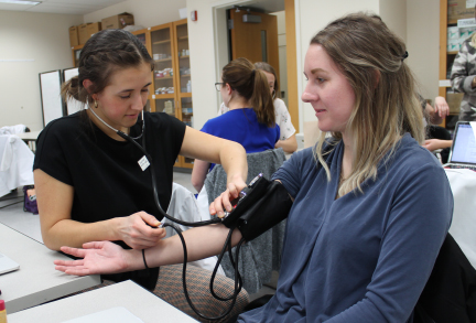 Students practice doing blood pressure checks on classmates in lab